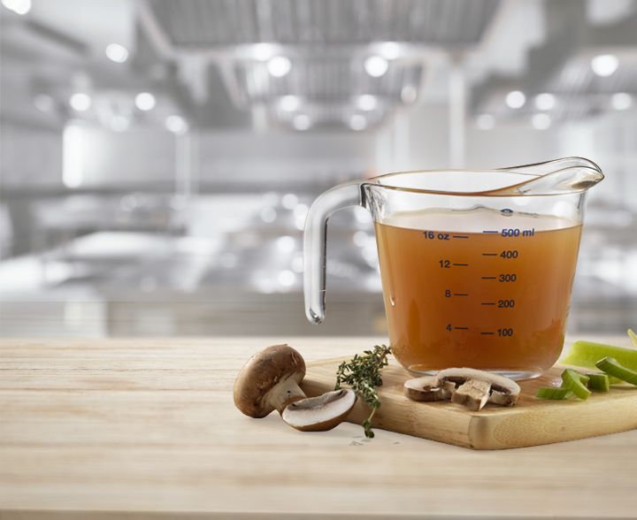 A copper saucepan of rich brown broth concentrate on a striped kitchen towel beside a spoon