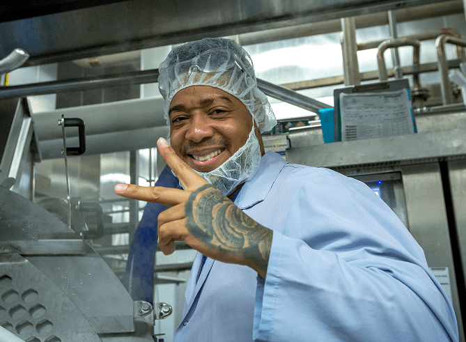A Kettle Cuisine production team member in a hairnet smiling beside packaging equipment