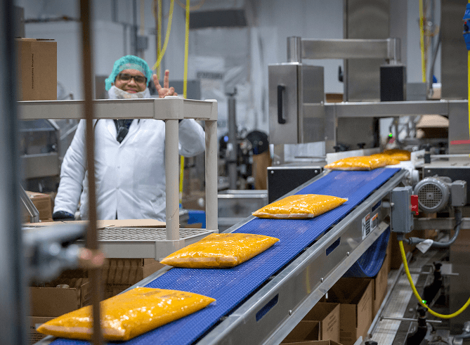 Pouches of sauce moving along a conveyor while a team member watches from the line