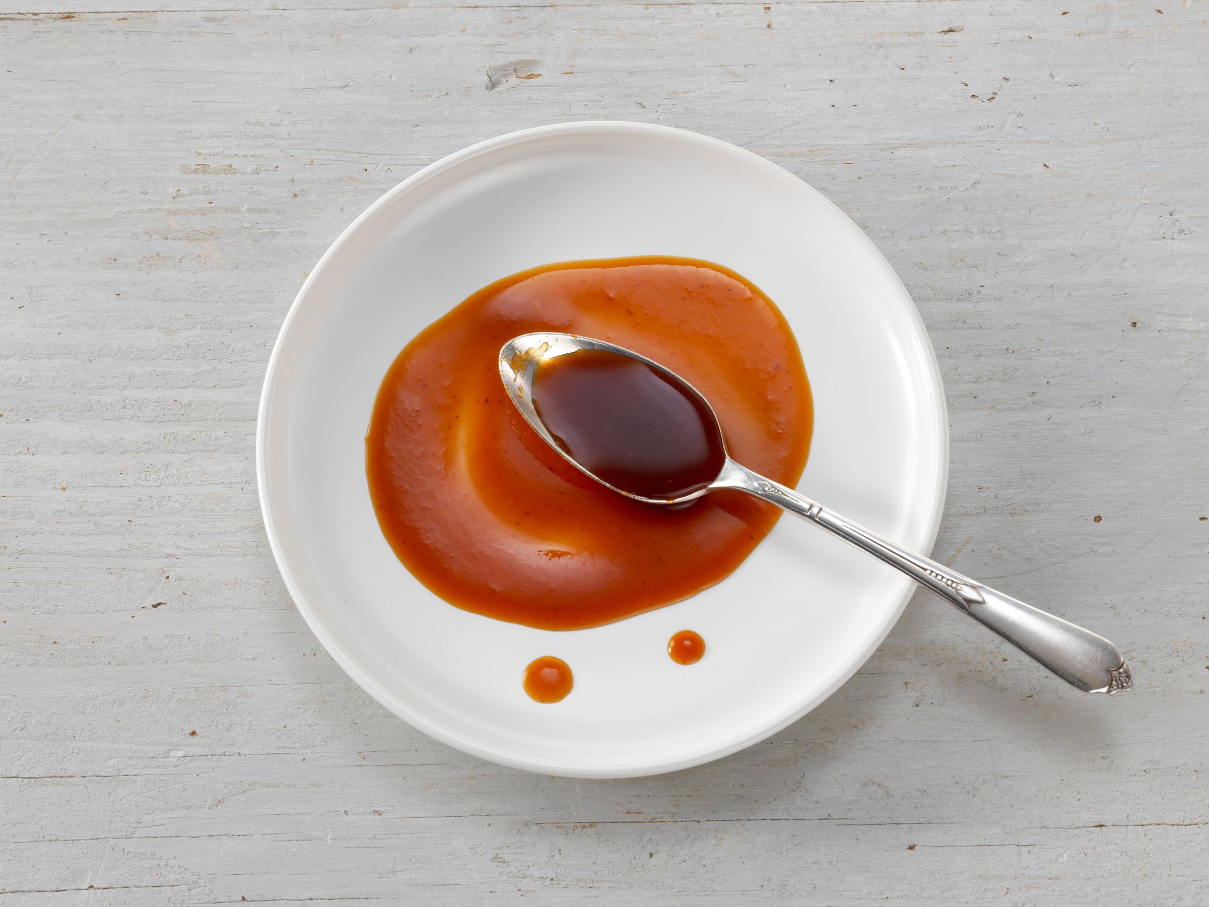 A spoon of rich demi-glace resting in a pool of sauce on a white plate