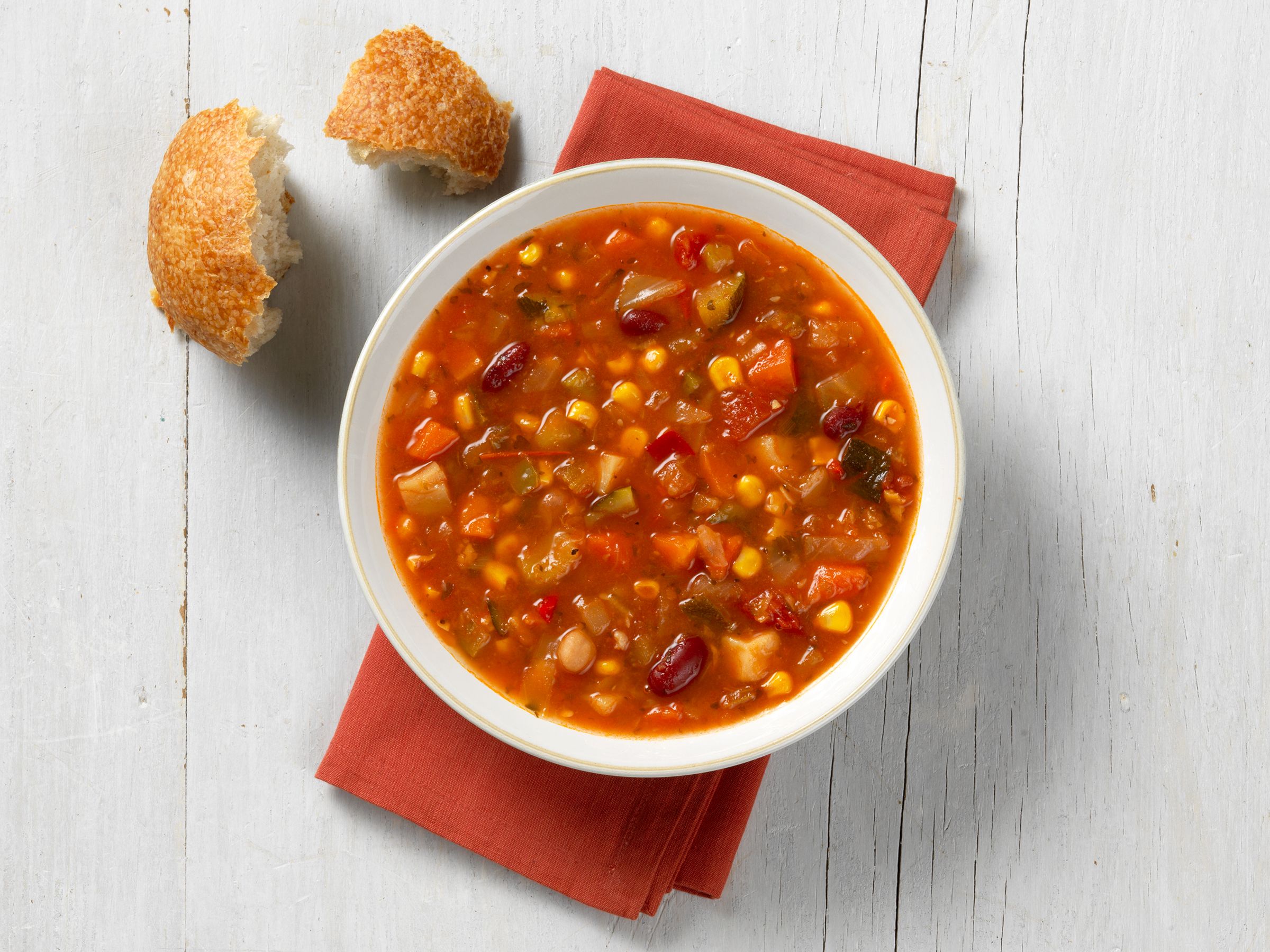 A bowl of Soup Supreme vegetable soup with a torn piece of crusty bread