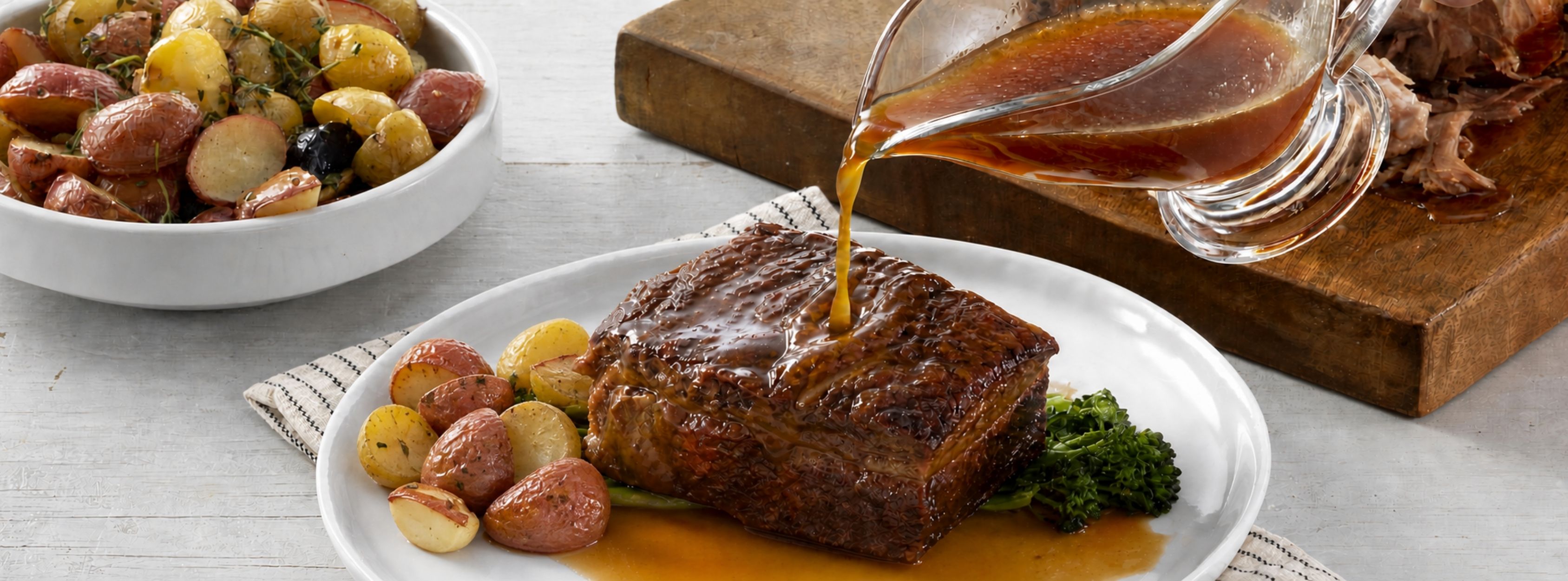 Pan gravy poured over sliced pork roast with broccolini and roasted potatoes